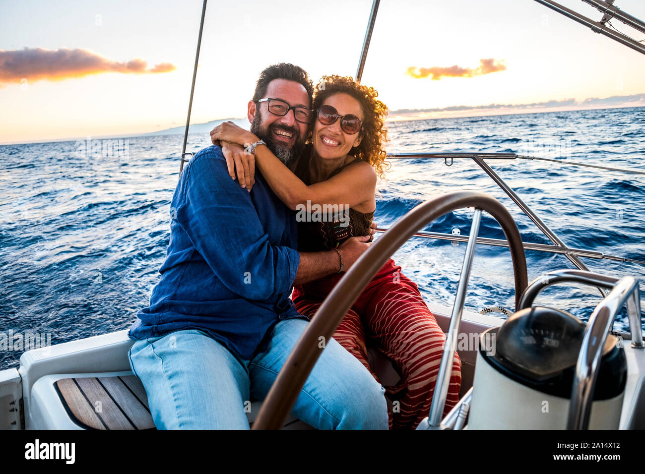 Happy people caucasian adult couple enjoy the sail boat trip on summer holiday vacation - outdoor leisure activity with ocean and sunset in. backgroun Stock Photo