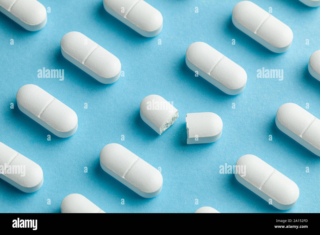 White pills on blue background. One tablet is broken in half, reducing the dose of the medicine. Stock Photo