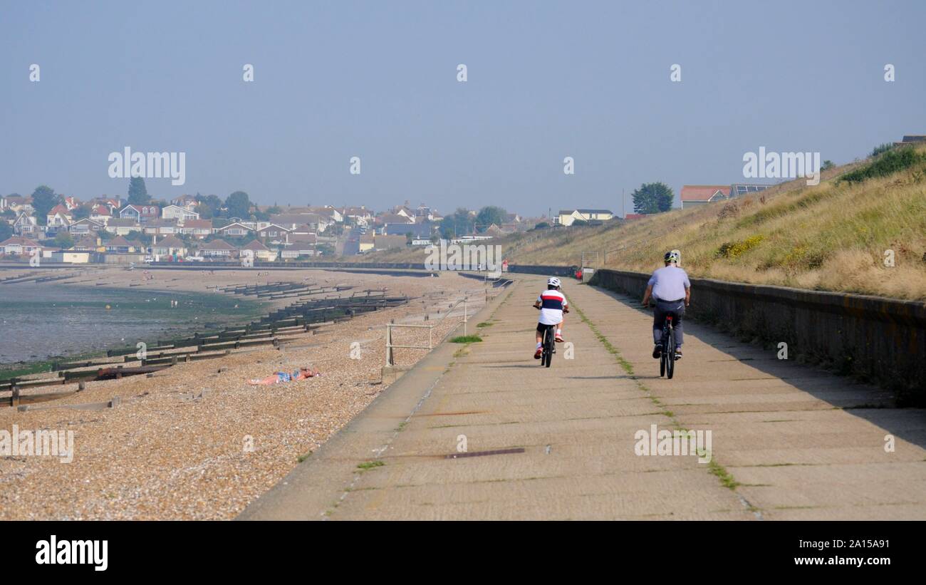 Cyclists on path along Studd Hill Beach with Herne Bay in background, Kent, UK. Stock Photo