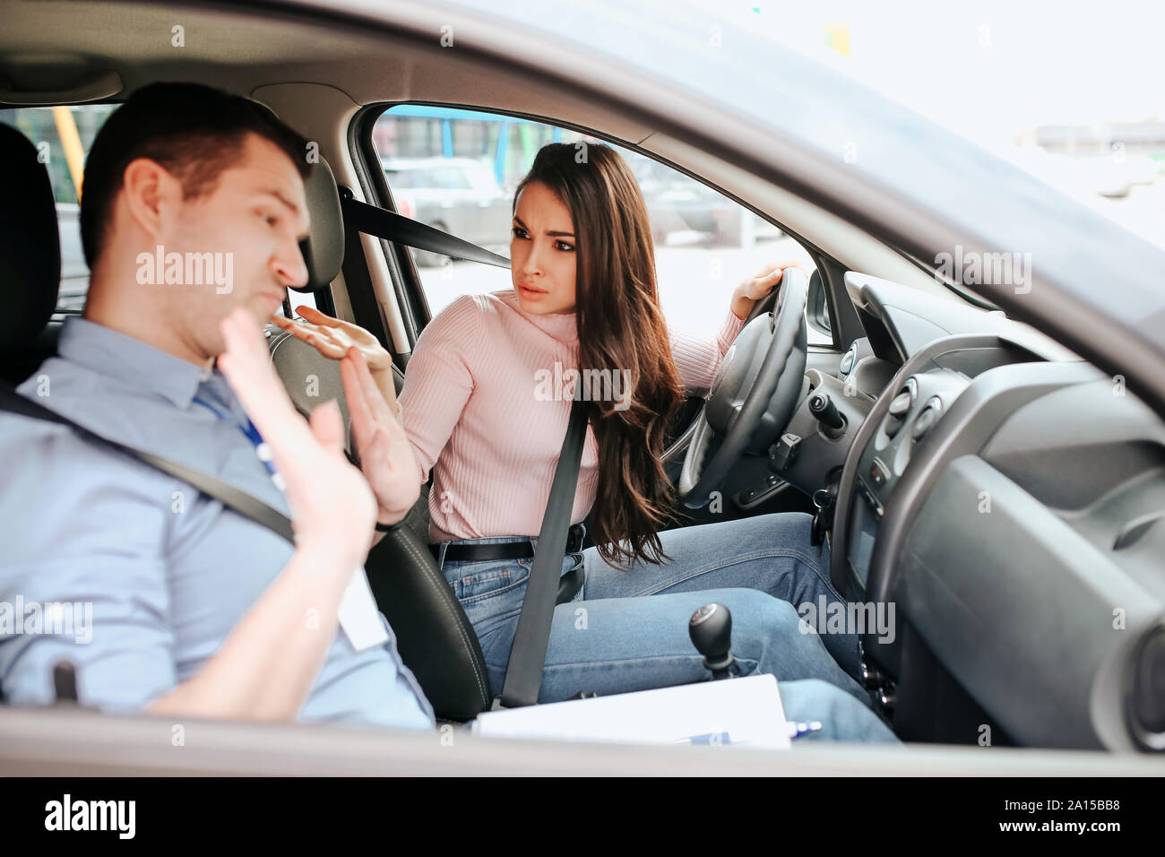 Male auto instructor takes exam in young woman. Female student look at teacher with confusion and misunderstanding. Guy show hands and look down. Dayl Stock Photo