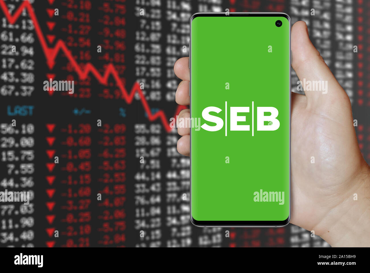 A man holds a smartphone displaying the logo of company SEB listed on OMX Stockholm. Negative stock market background. Credit: PIXDUCE Stock Photo