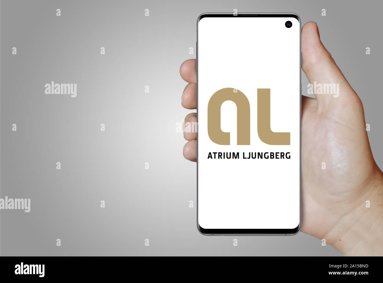 A man holds a smartphone displaying the logo of company Atrium Ljungberg listed on OMX Stockholm. Grey gradient in the background. Credit: PIXDUCE Stock Photo