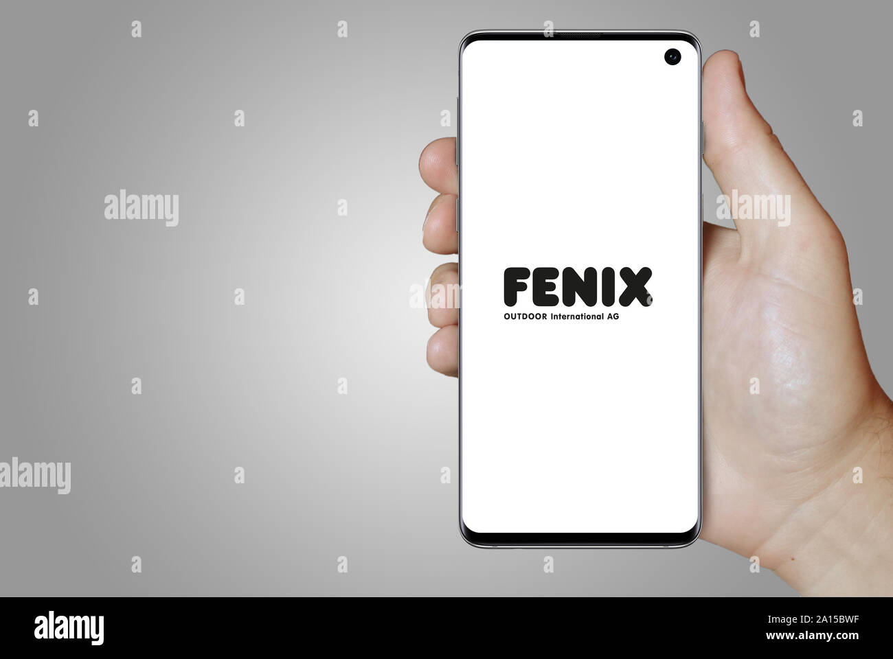 A man holds a smartphone displaying the logo of company Fenix Outdoor listed on OMX Stockholm. Grey gradient in the background. Credit: PIXDUCE Stock Photo