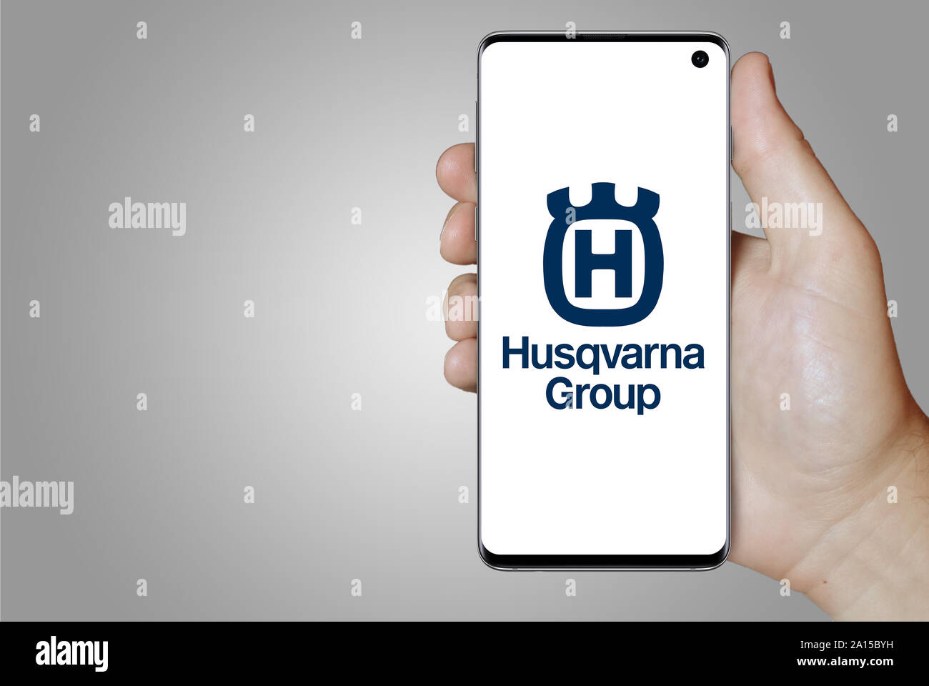 A man holds a smartphone displaying the logo of company Husqvarna listed on OMX Stockholm. Grey gradient in the background. Credit: PIXDUCE Stock Photo