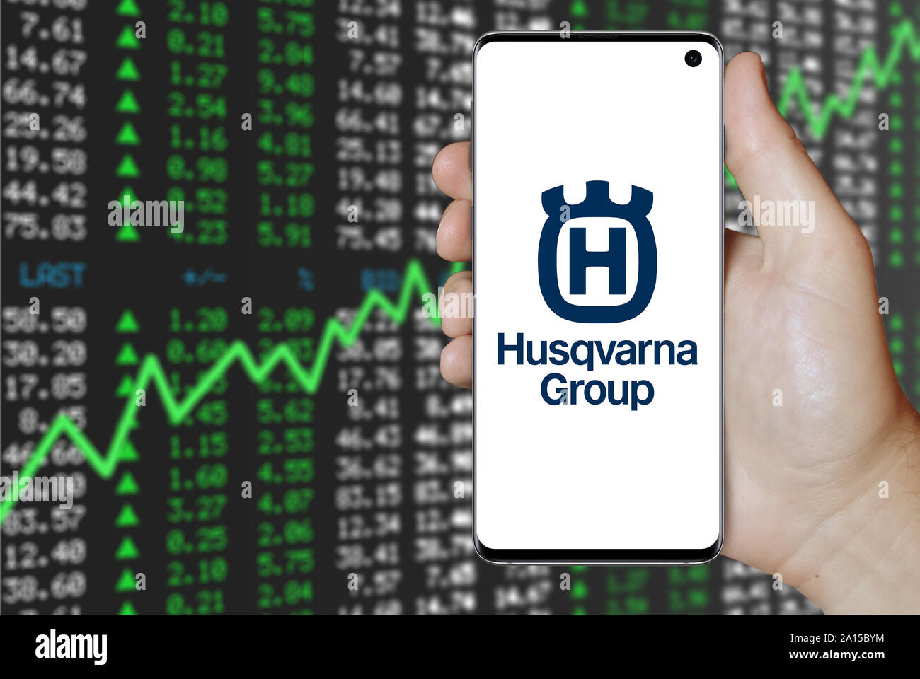 A man holds a smartphone displaying the logo of company Husqvarna listed on OMX Stockholm. Positive stock market background. Credit: PIXDUCE Stock Photo