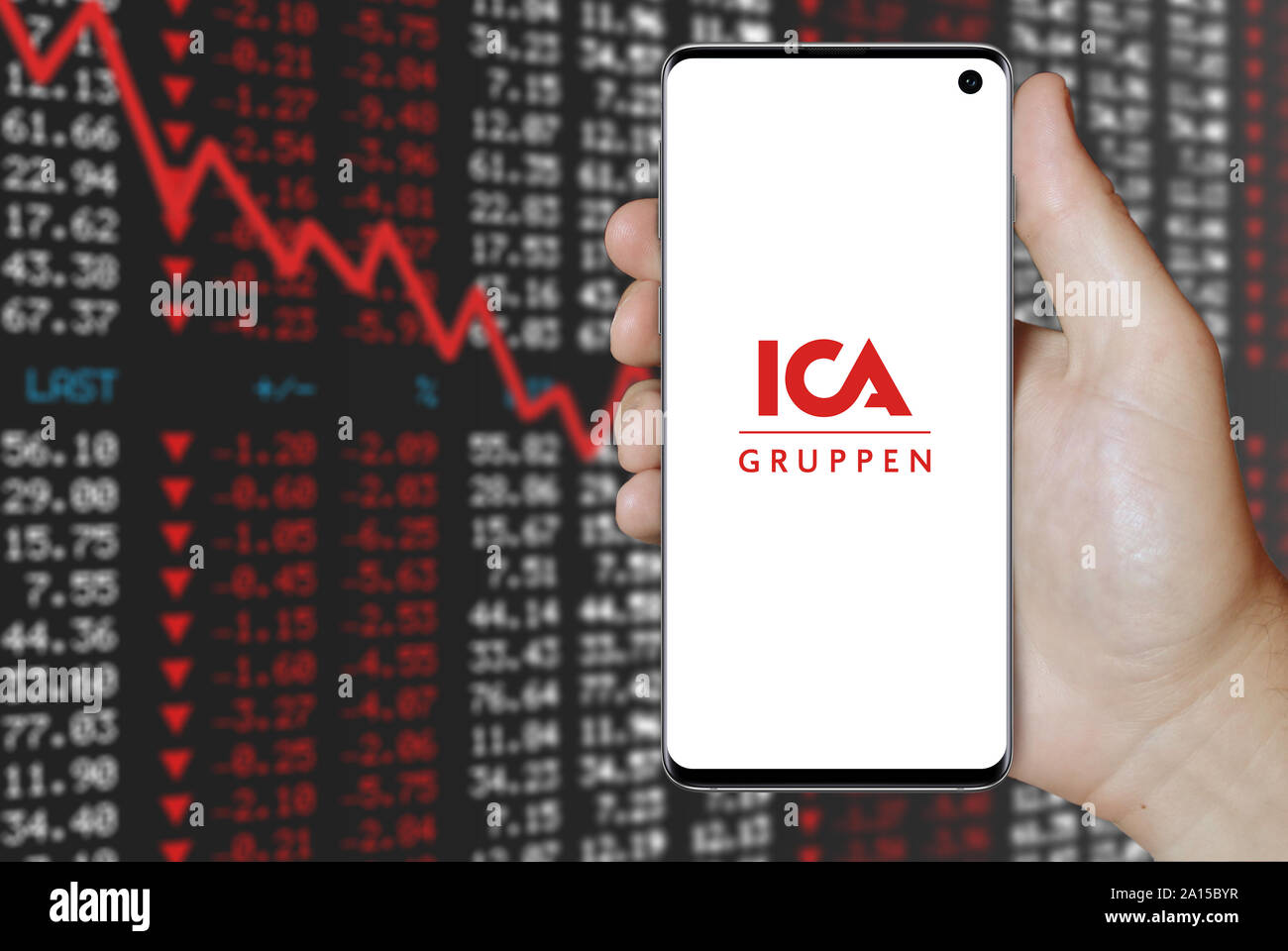 A man holds a smartphone displaying the logo of company ICA Gruppen listed on OMX Stockholm. Negative stock market background. Credit: PIXDUCE Stock Photo