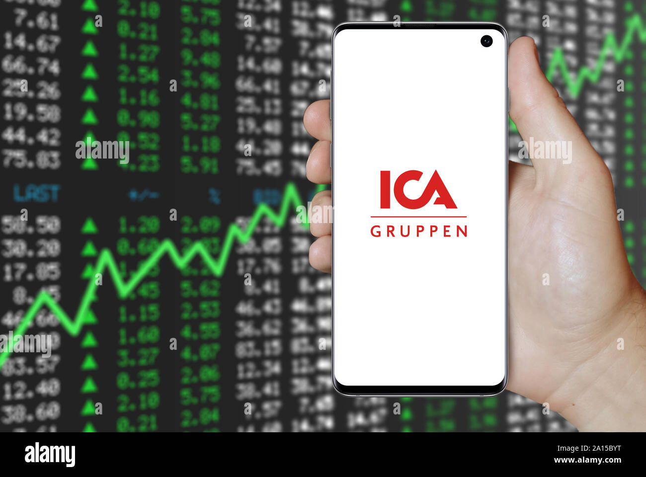 A man holds a smartphone displaying the logo of company ICA Gruppen listed on OMX Stockholm. Positive stock market background. Credit: PIXDUCE Stock Photo