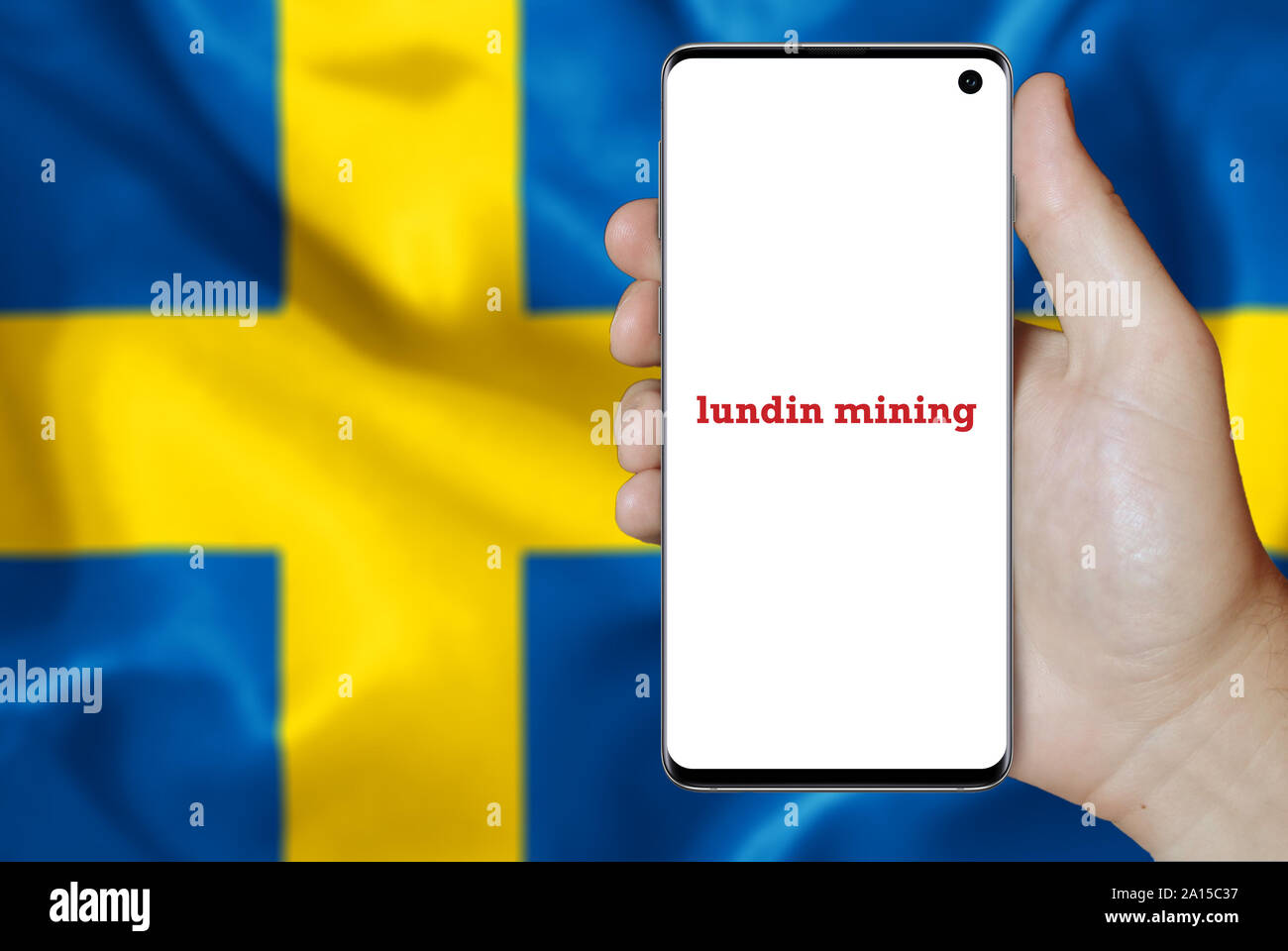 A man holds a smartphone displaying the logo of company Lundin Mining listed on OMX Stockholm. Swedish flag in the background. Credit: PIXDUCE Stock Photo