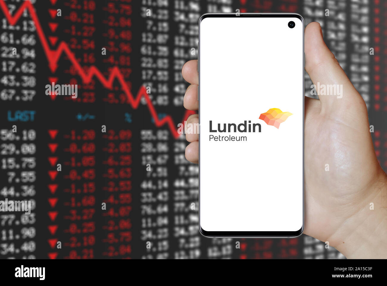 A man holds a smartphone displaying the logo of company Lundin Petroleum listed on OMX Stockholm. Negative stock market background. Credit: PIXDUCE Stock Photo