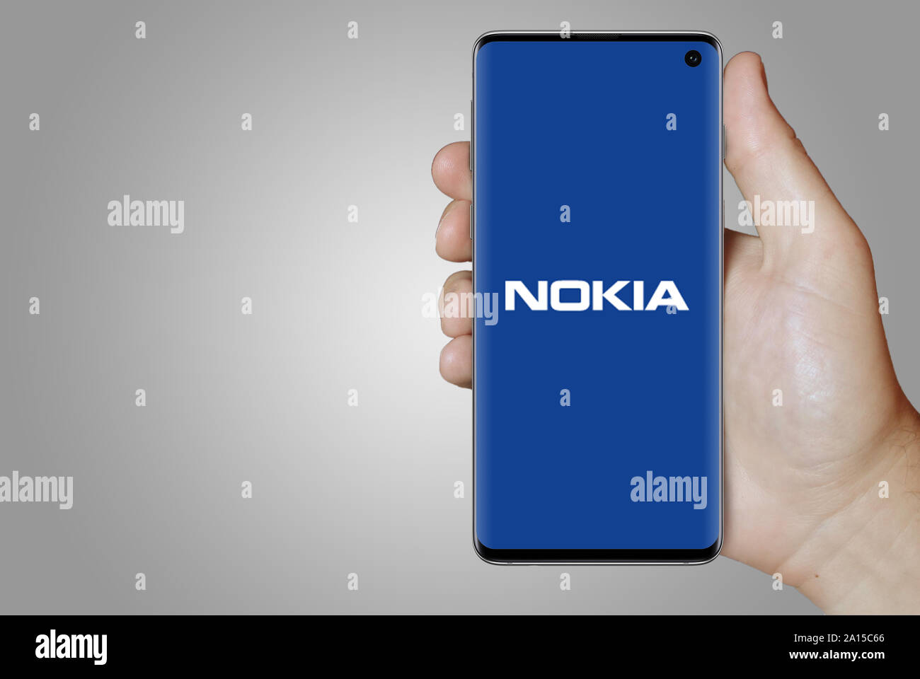 A man holds a smartphone displaying the logo of company Nokia listed on OMX Stockholm. Grey gradient in the background. Credit: PIXDUCE Stock Photo