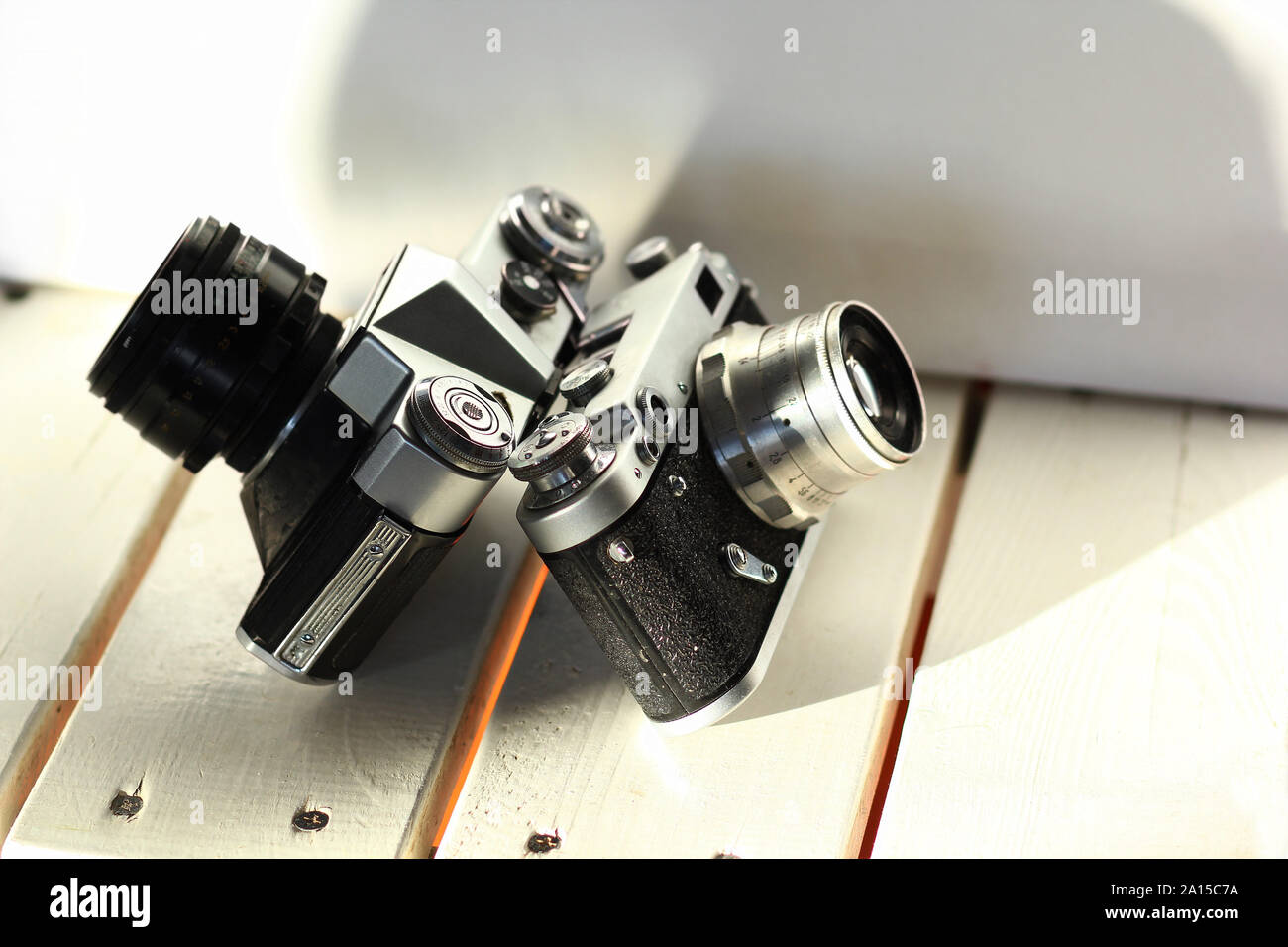 Two black old-school vintage film photo cameras on white wooden planks, sunlit interior Stock Photo