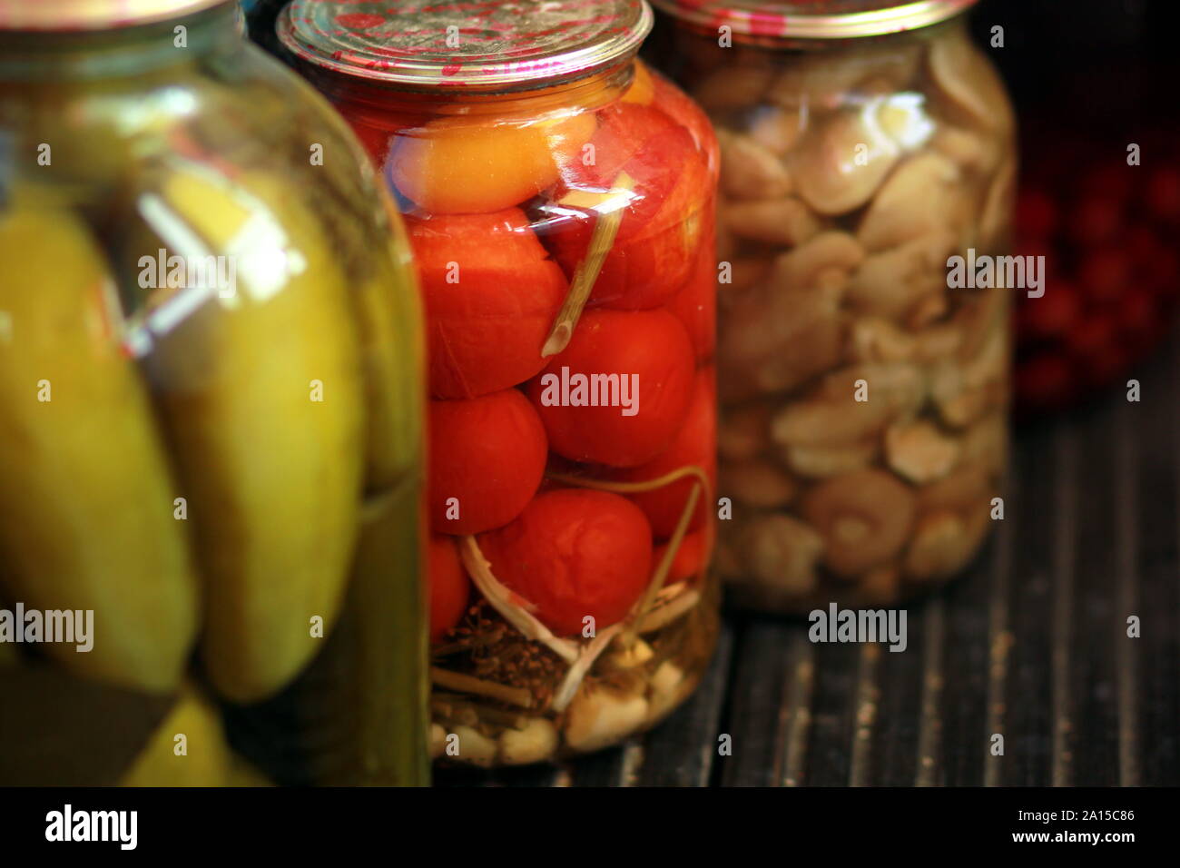 Row of jars with pickled tomatoes, cucumbers and mushrooms standing on black wooden floor Stock Photo