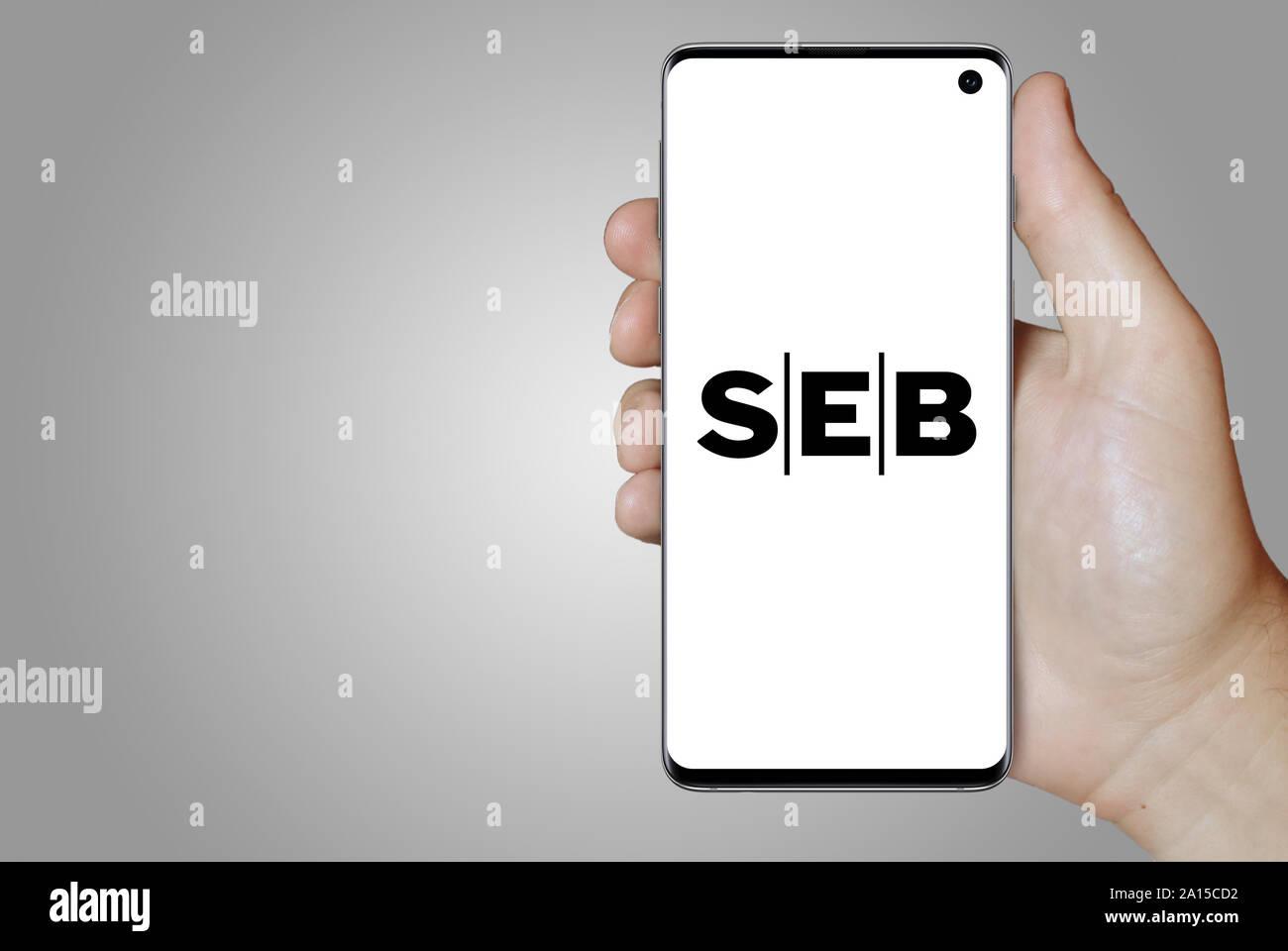 A man holds a smartphone displaying the logo of company SEB listed on OMX Stockholm. Grey gradient in the background. Credit: PIXDUCE Stock Photo