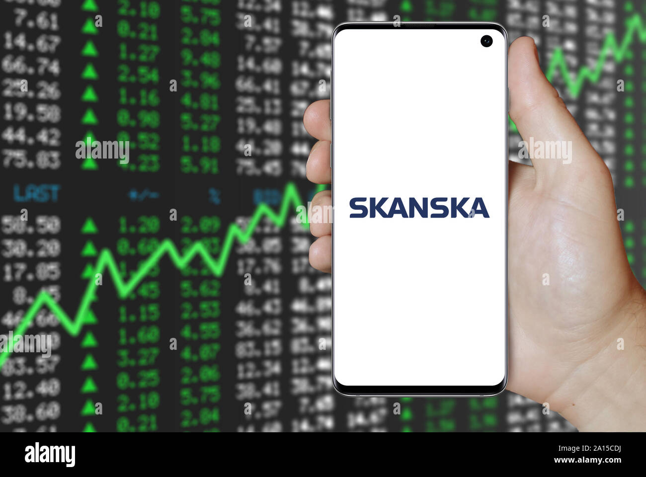 A man holds a smartphone displaying the logo of company Skanska listed on OMX Stockholm. Positive stock market background. Credit: PIXDUCE Stock Photo