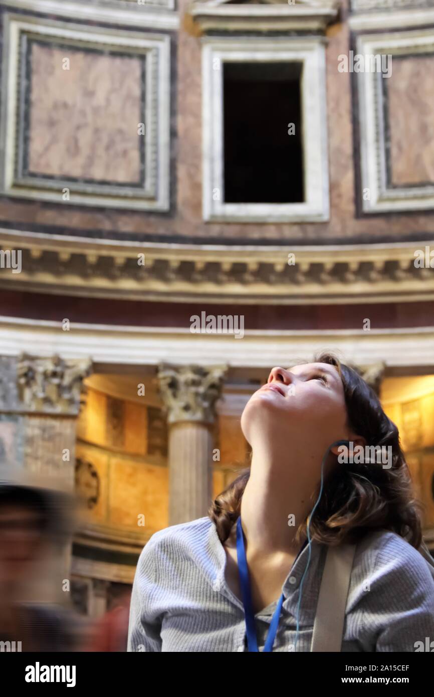 Young woman tourist looking above and admiring the beauty of Pantheon in Rome, Italy. On excursion with audio guide and headphones Stock Photo