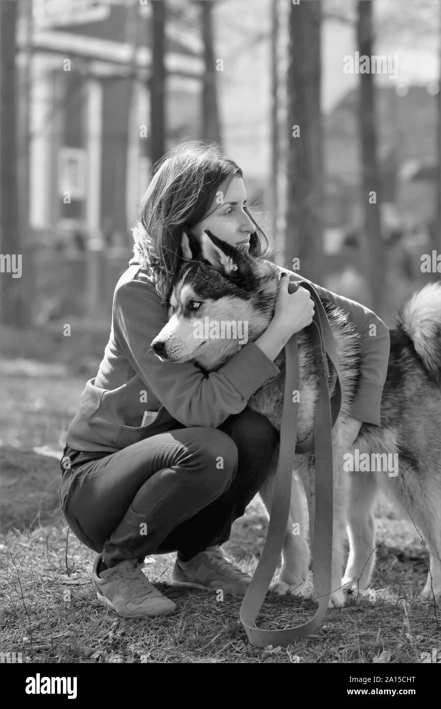 Black and white portrait of a sad woman saying goodbye to her husky sled dog pet Stock Photo