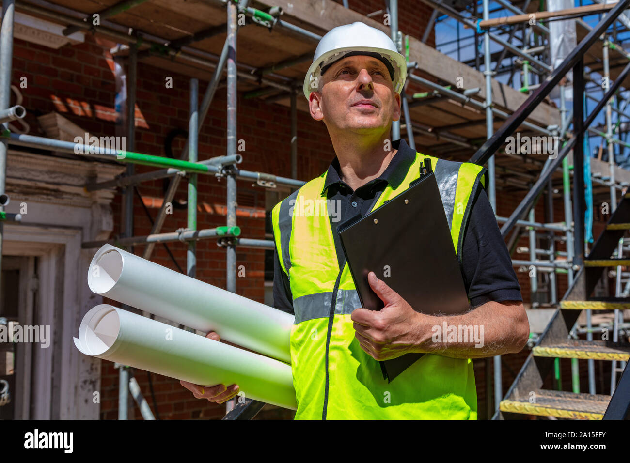 Male builder foreman, worker, surveyor, engineer or architect on construction site holding building plans and clipboard Stock Photo