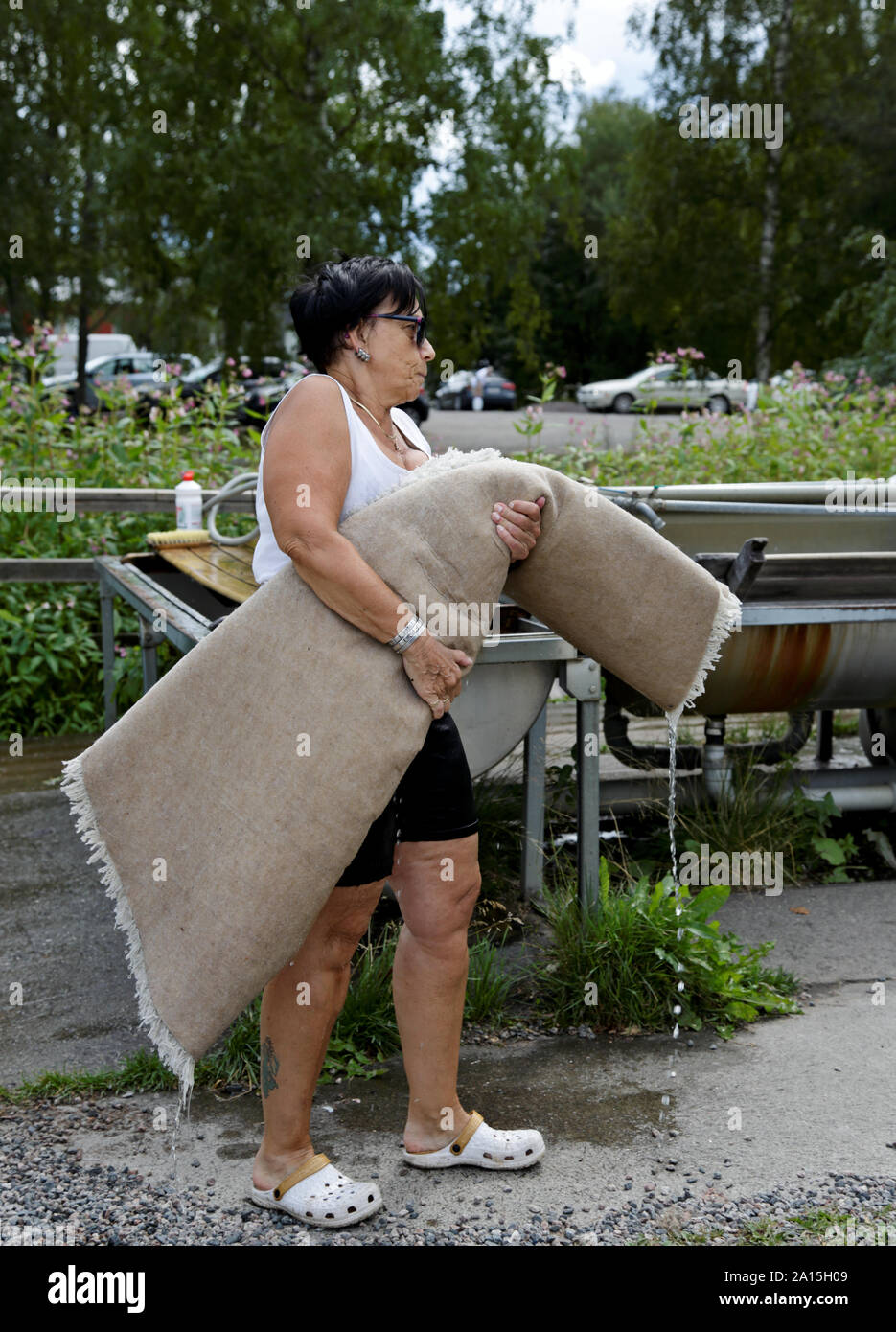 Hameenlinna, FINLAND 08/04/2018 A woman carrying just washed heavy carpet to  a dryer and then to rack to drip and dry. Stock Photo