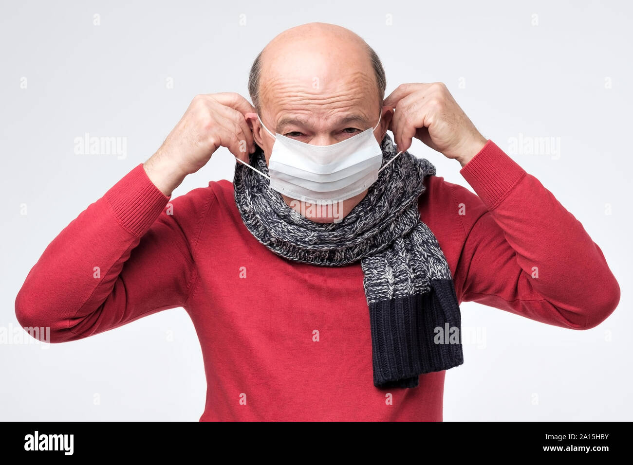 Caucasian mature man closing face with medical mask protecting from smog or virus. Studio shot Stock Photo