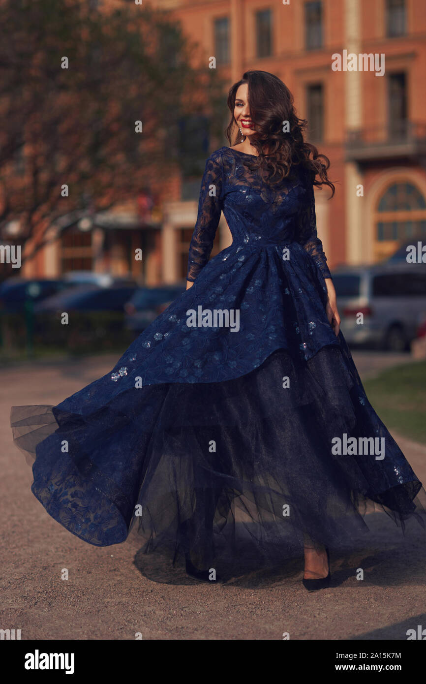 Elegant woman in blue ball gown dress standing and posing on a sunny evening  at city street. Fashion model full length portrait Stock Photo - Alamy