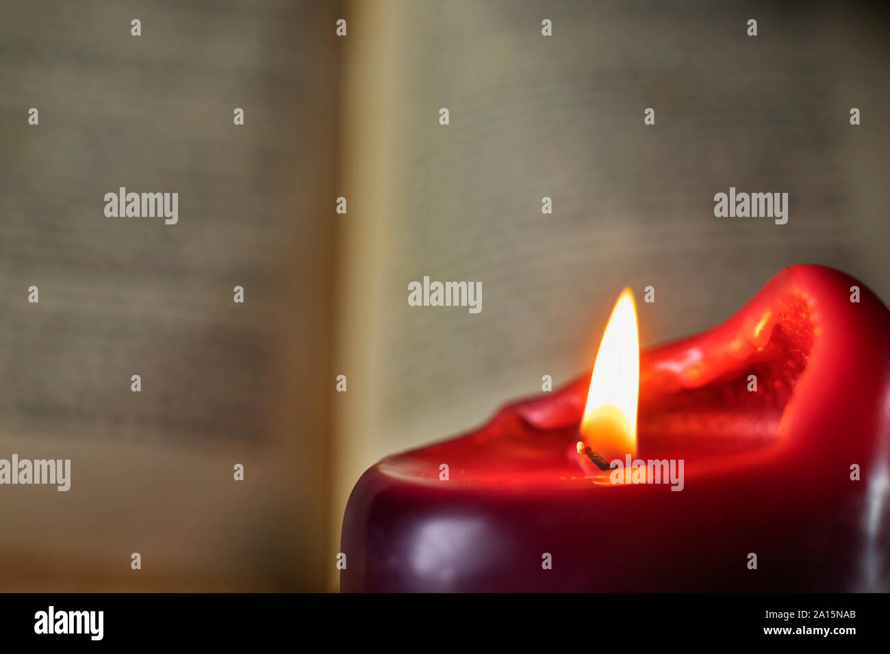 Reading under lighted candle , in the foreground one red candle ,in the background an opened book out of focus Stock Photo