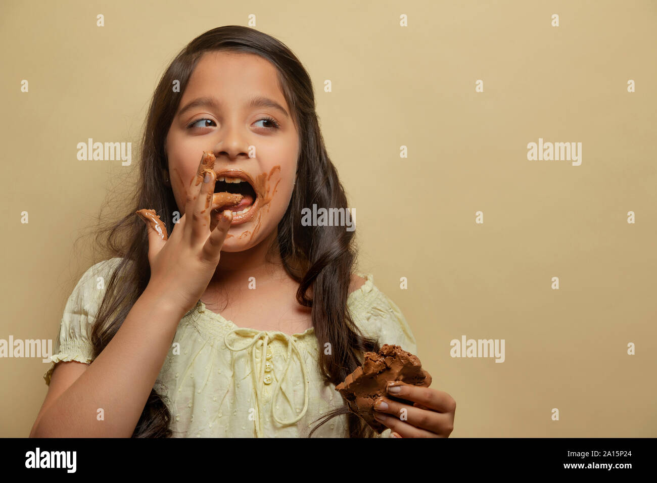 Girl licking chocolate from fingers holding a chocolate bar in the other hand looking away Stock Photo