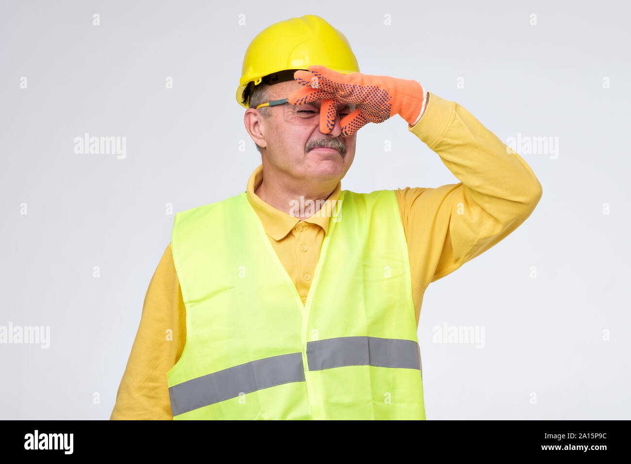 Displeased mature road worker in helmet and protective gloves closes nose because of unpleasant smell. Sewage problem. Stock Photo