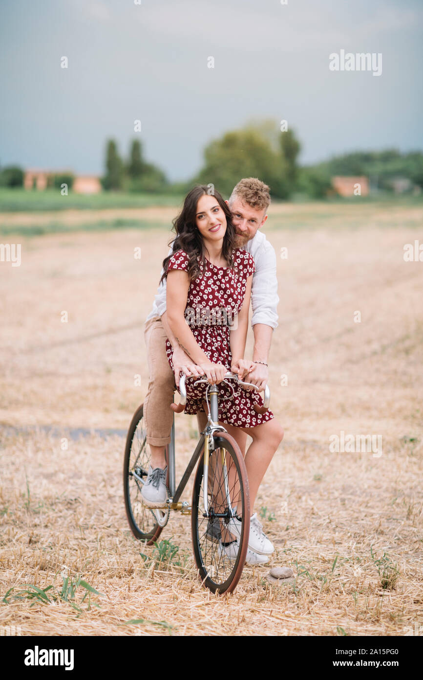 Portrait of couple on handcrafted racing cycle on stubble field Stock Photo