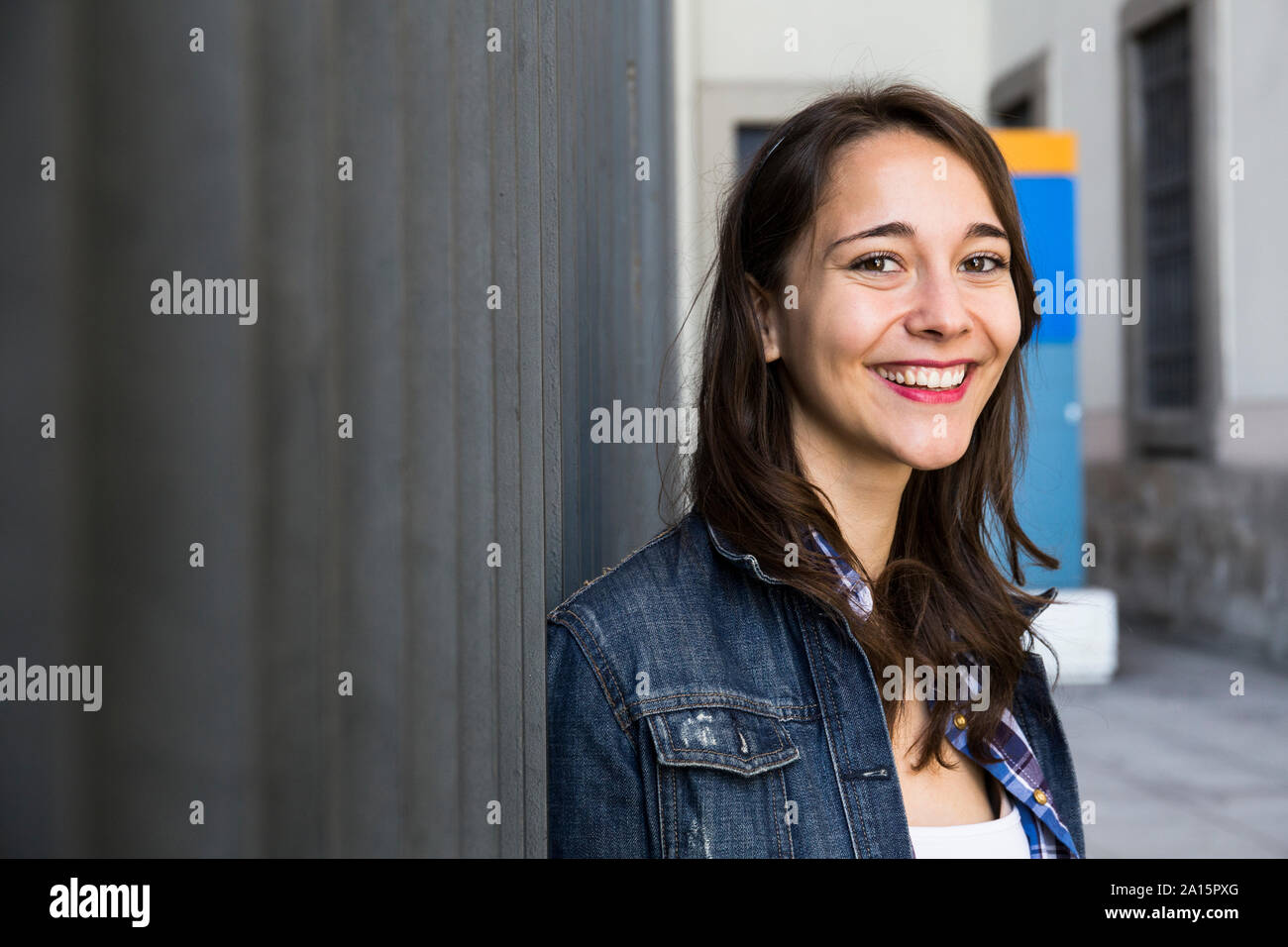 Young smiling woman looking at camera, standing at wall Stock Photo