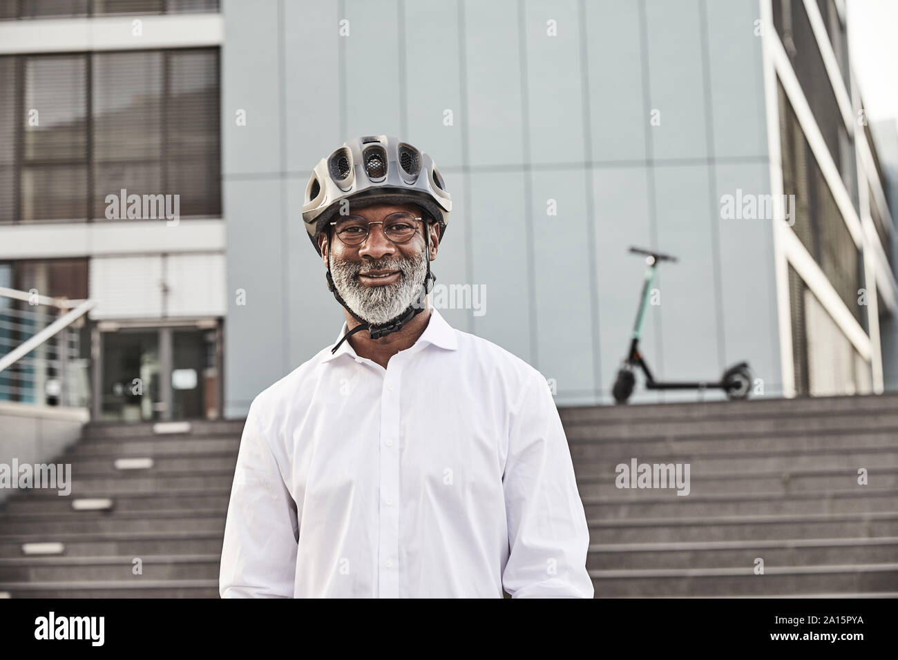 Portrait of smiling mature businessman with E-Scooter wearing cycling helmet Stock Photo