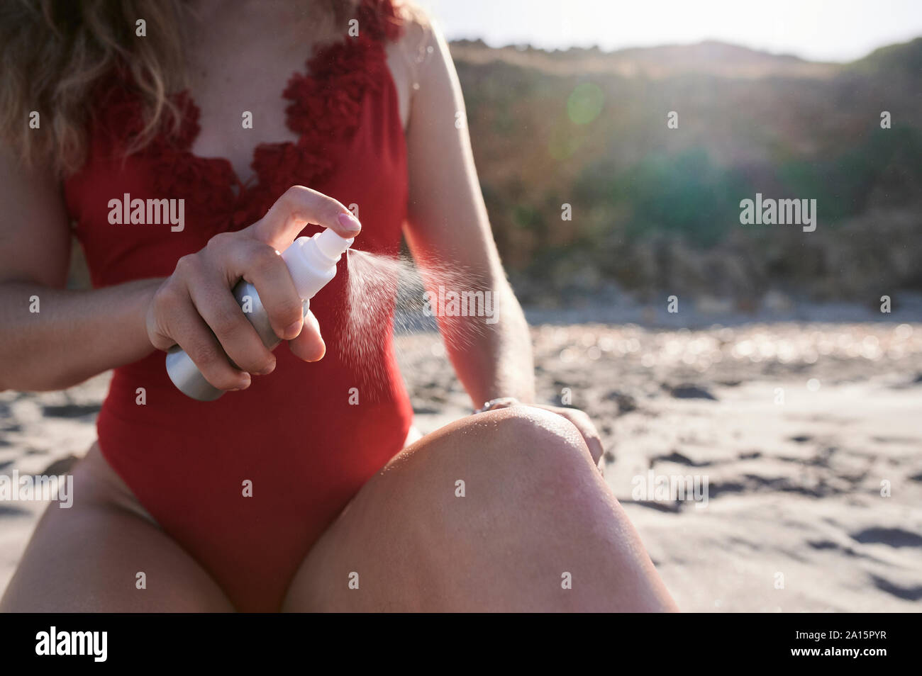 Young woman applying suncream spray on the beach Stock Photo