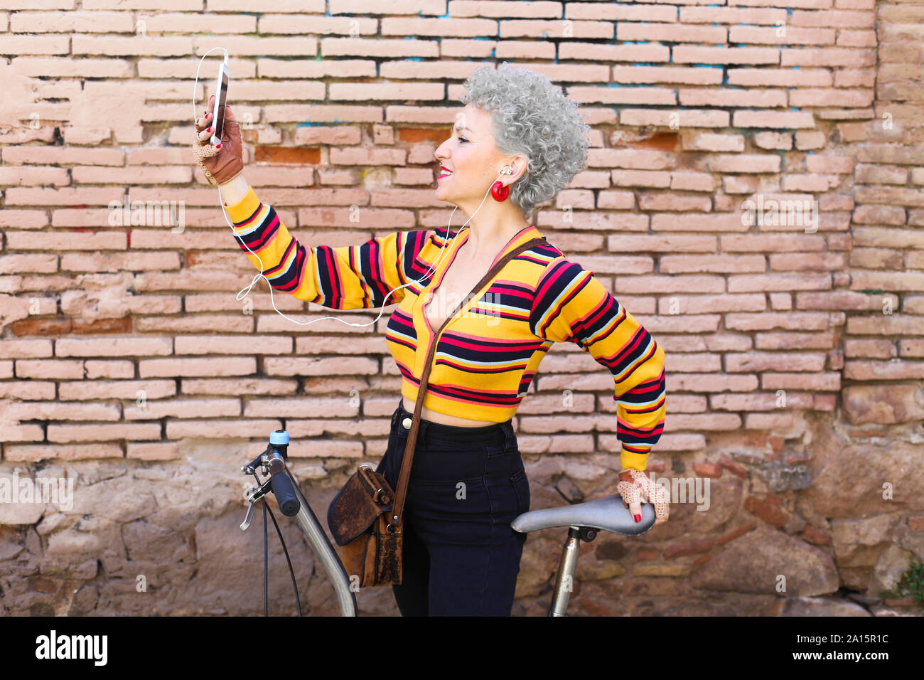 Smiling mature woman with bicycle taking selfie with cell phone Stock Photo