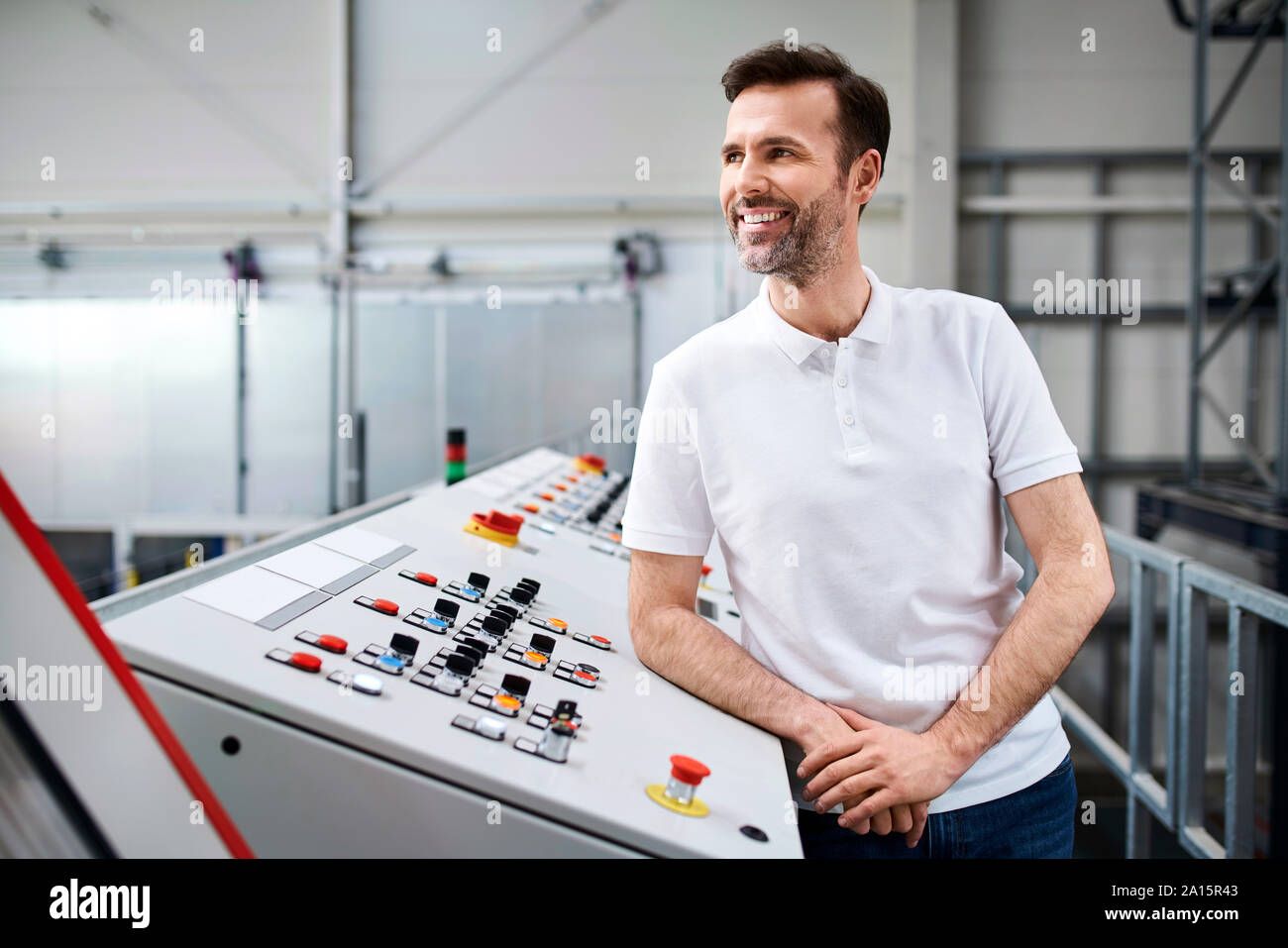 Smiling man standing at control panel in a factory Stock Photo