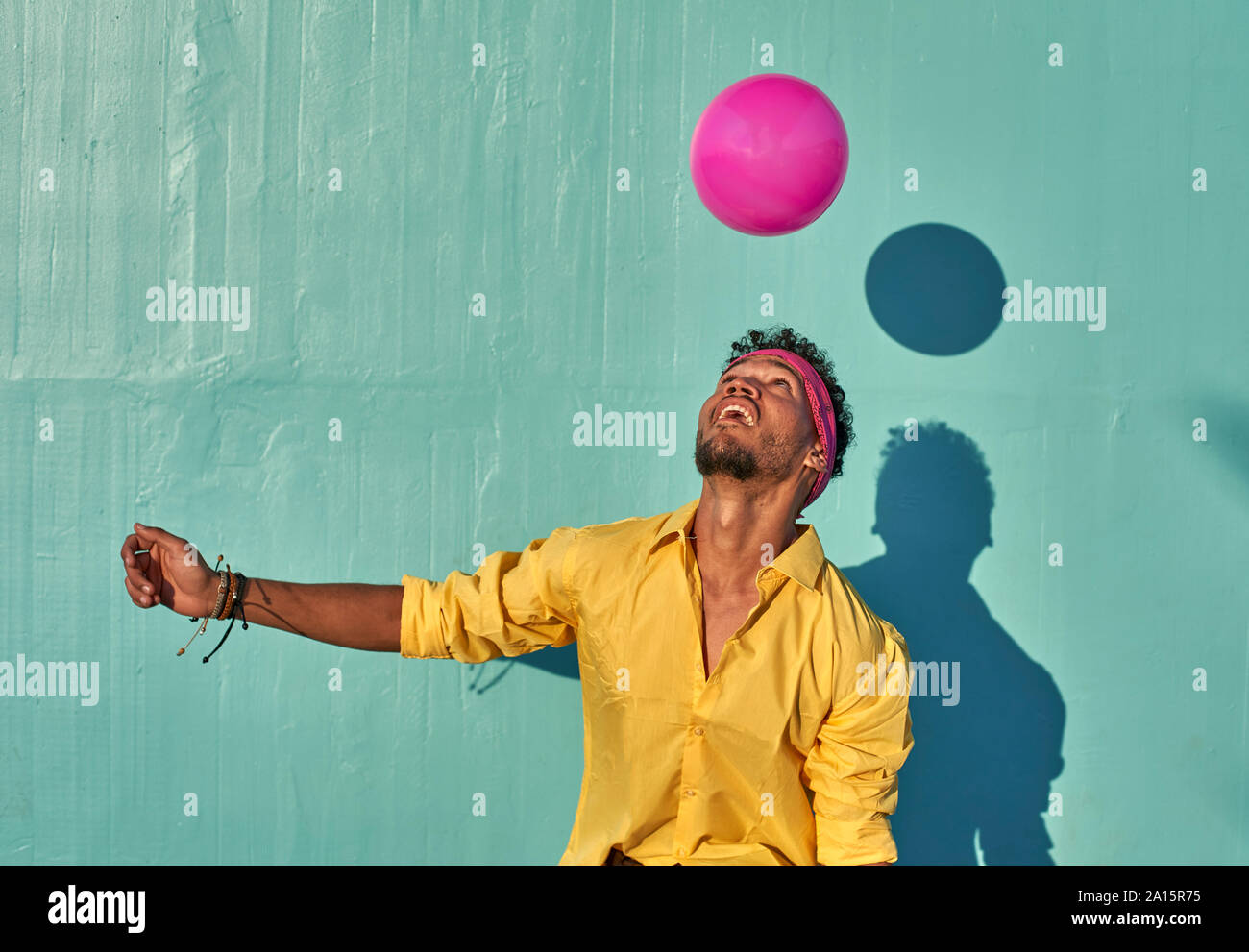 Young black man playing with a pink ball in front of a blue wall Stock Photo