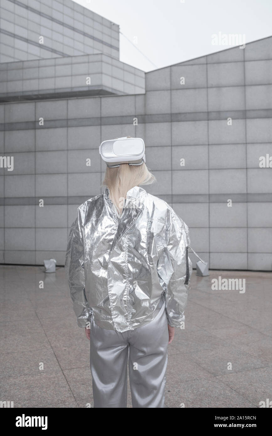 Rear view of girl in silver suit wearing VR goggles on back of head Stock Photo