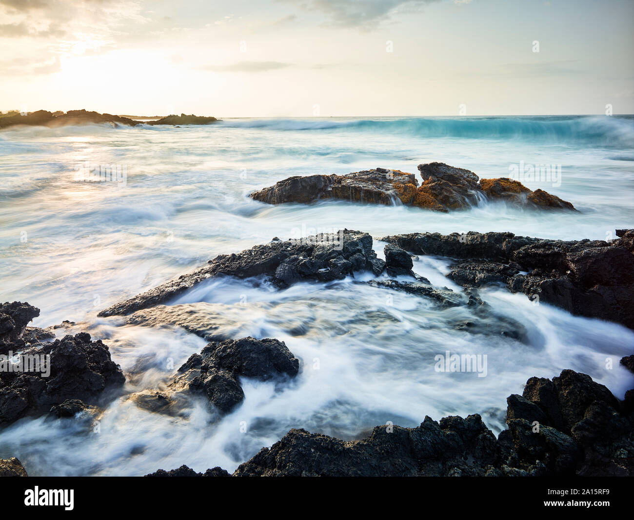 Waves splashing in Kealakekua Bay against cloudy sky during sunset Stock Photo