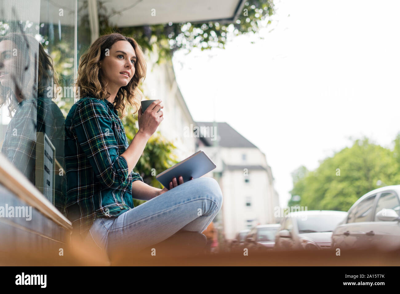Young woman sitting infront of coffee shop, using digital tablet, drinking coffee Stock Photo