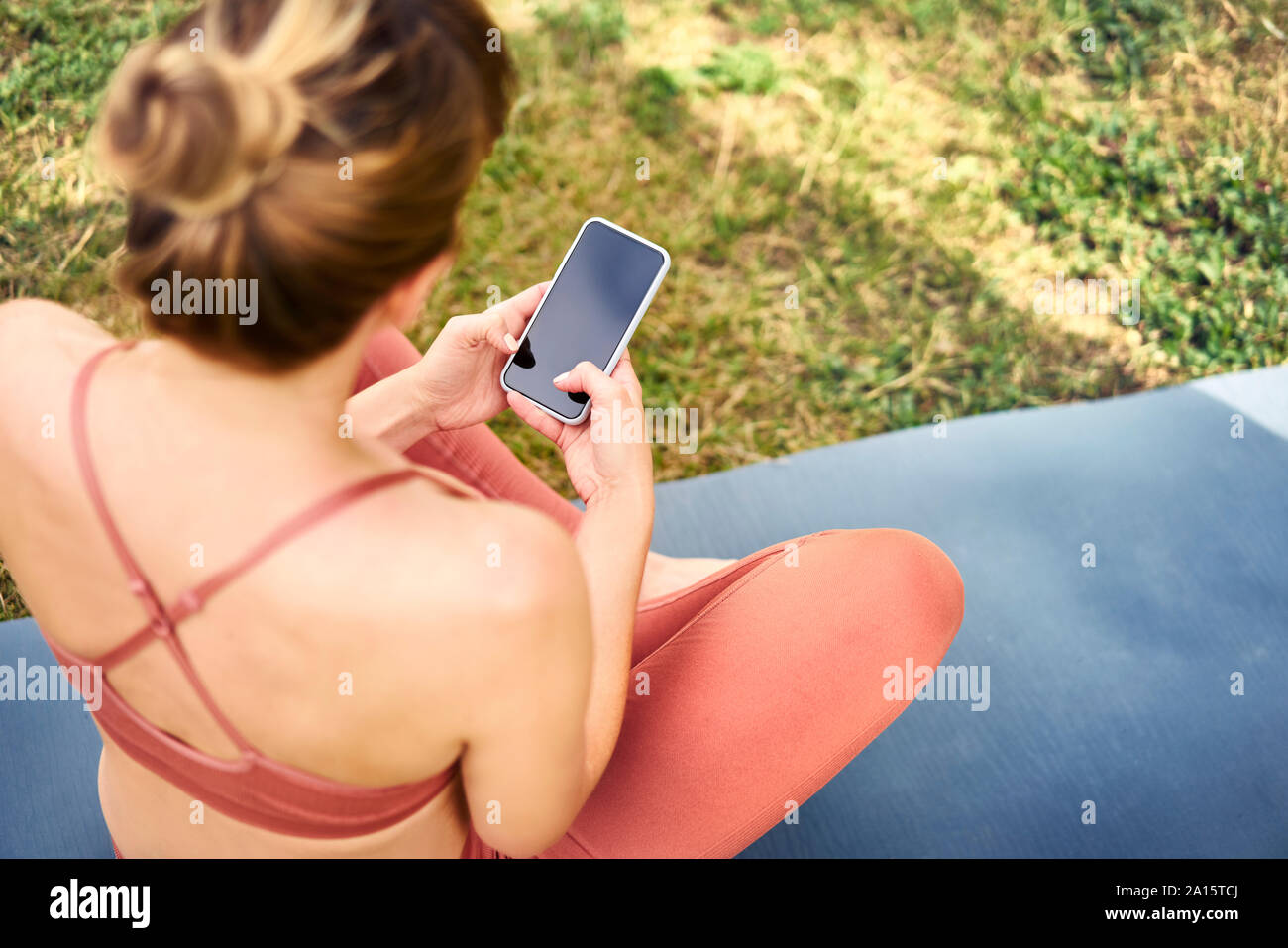 Woman using smartphone while taking a break from practicing yoga outdoors Stock Photo