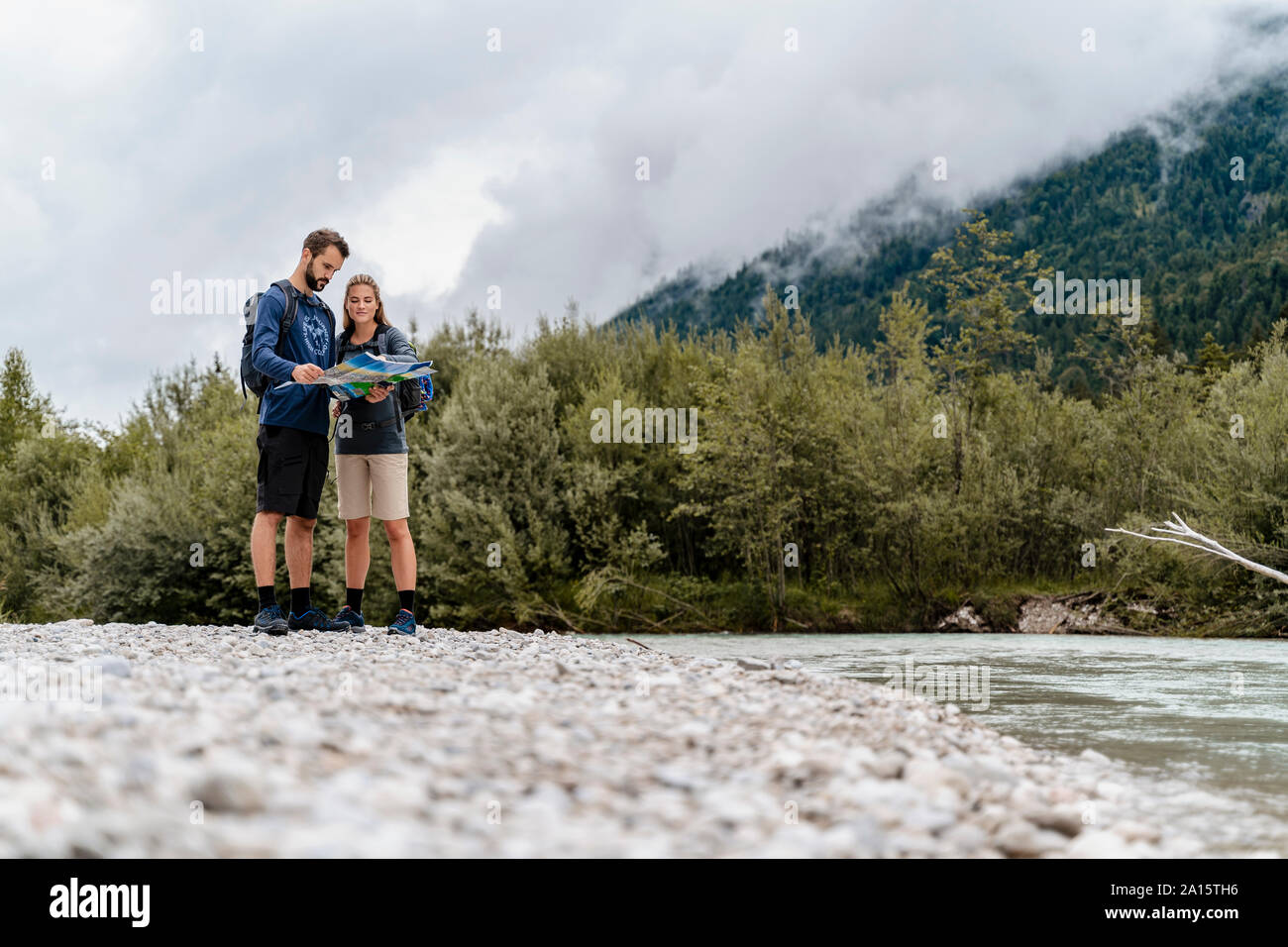 Young couple on a hiking trip at riverside reading map, Vorderriss, Bavaria, Germany Stock Photo