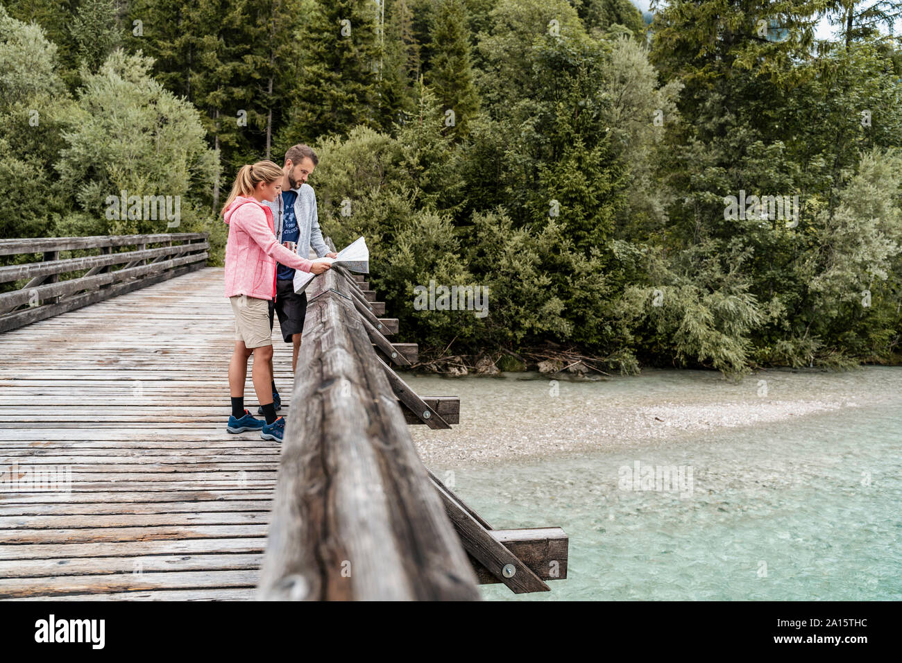 Young couple on a hiking trip reading map on wooden bridge, Vorderriss, Bavaria, Germany Stock Photo