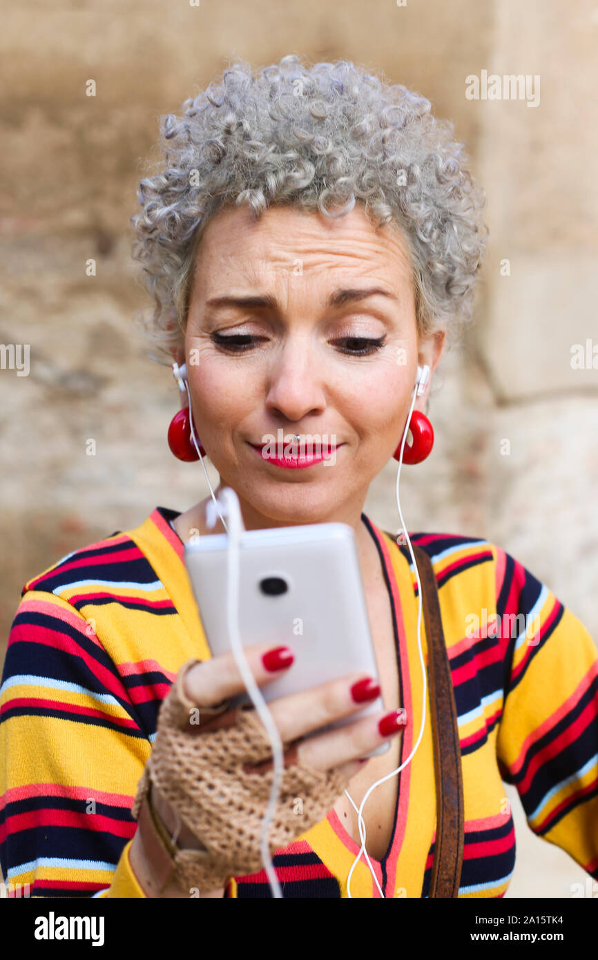 Portrait of pierced mature woman with grey curly hair looking at cell phone Stock Photo
