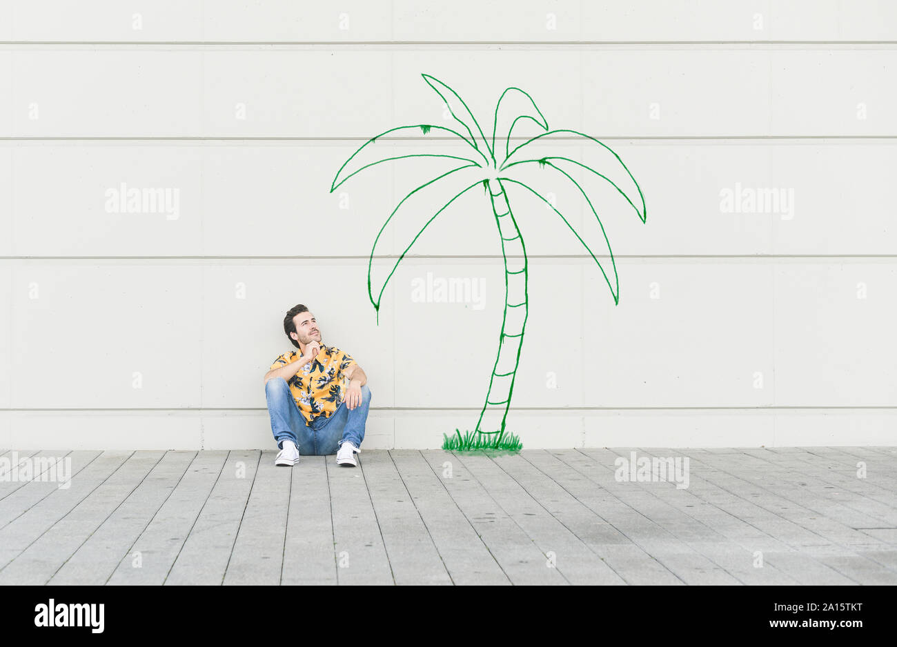 Digital composite of young man sitting at a palm at a wall Stock Photo