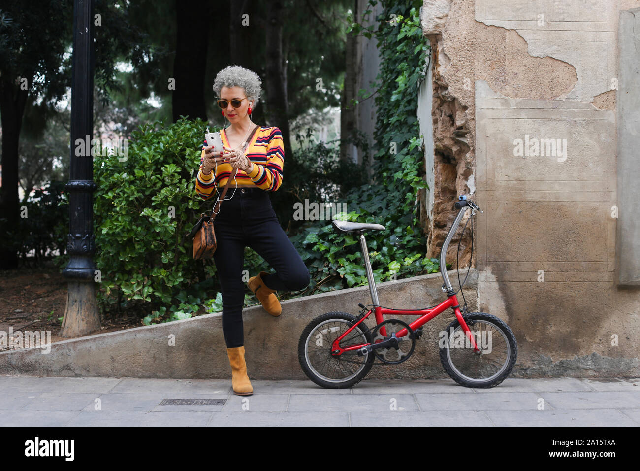 Fashionable mature woman with bicycle using smartphone on the street Stock Photo