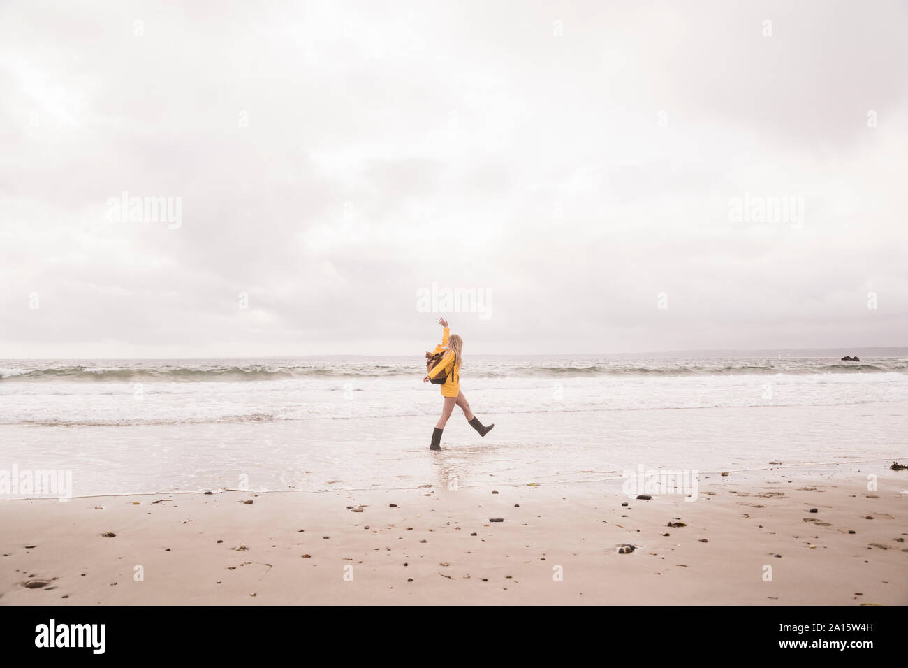 Woman wearing yellow rain jacket walking at the beach Stock Photo