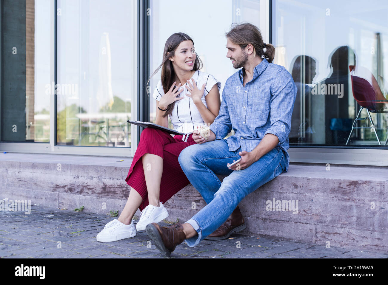 Young couple sitting on windowsill at a building using a tablet Stock Photo