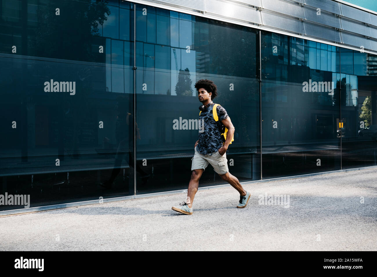 Man with yellow backpack and headphones walking down the street, Barcelona, Spain Stock Photo