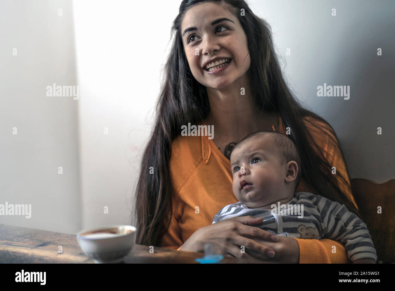 Happy mother with baby sitting at wooden table at home Stock Photo