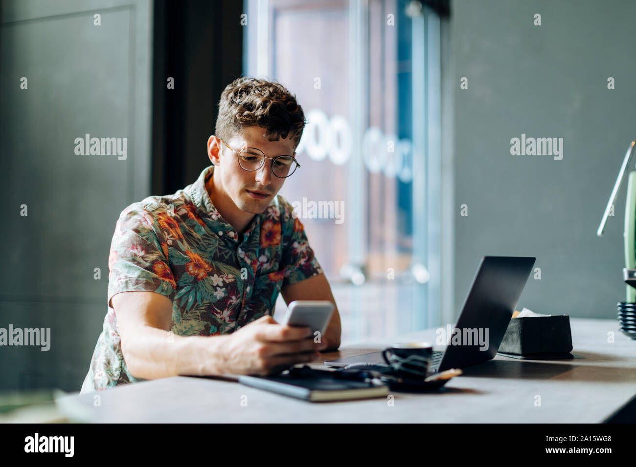 Young man sitting in cafe, using samrtphone and laptop Stock Photo