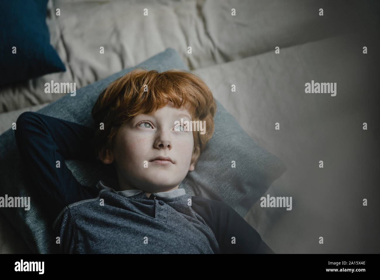 Portrait of redheaded boy lying on couch looking at distance Stock Photo