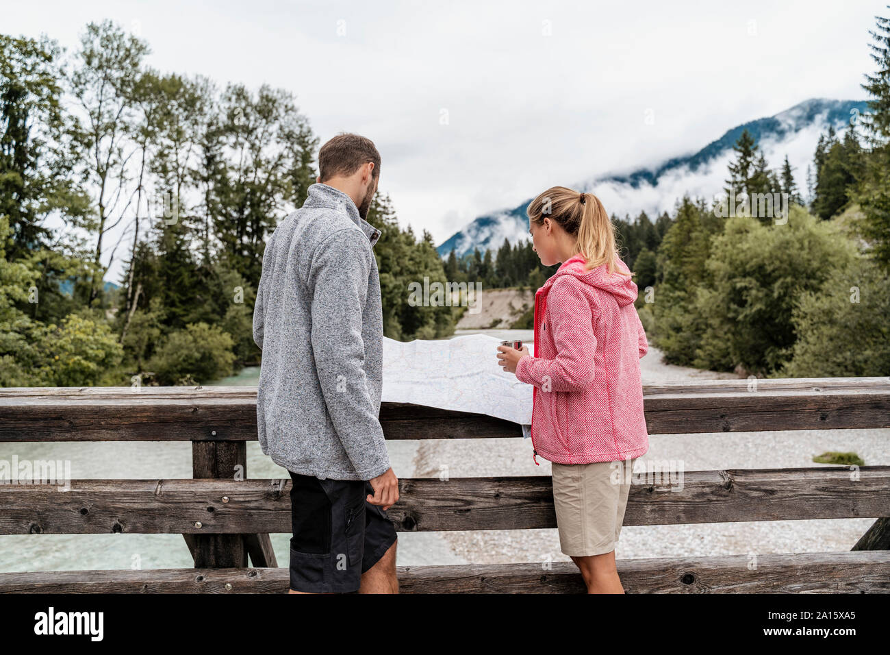 Young couple on a hiking trip reading map on wooden bridge, Vorderriss, Bavaria, Germany Stock Photo